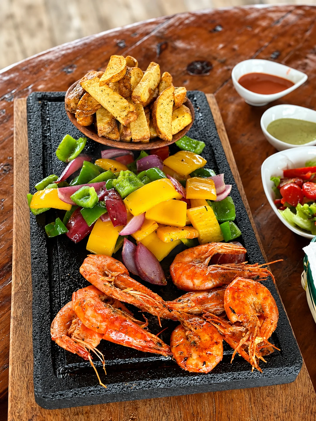 Camarones con vegetales sobre piedra volcánica, papas y salsas